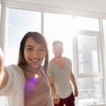 Young Couple Taking Selfie Photo Holding Hands In Kitchen, Asian